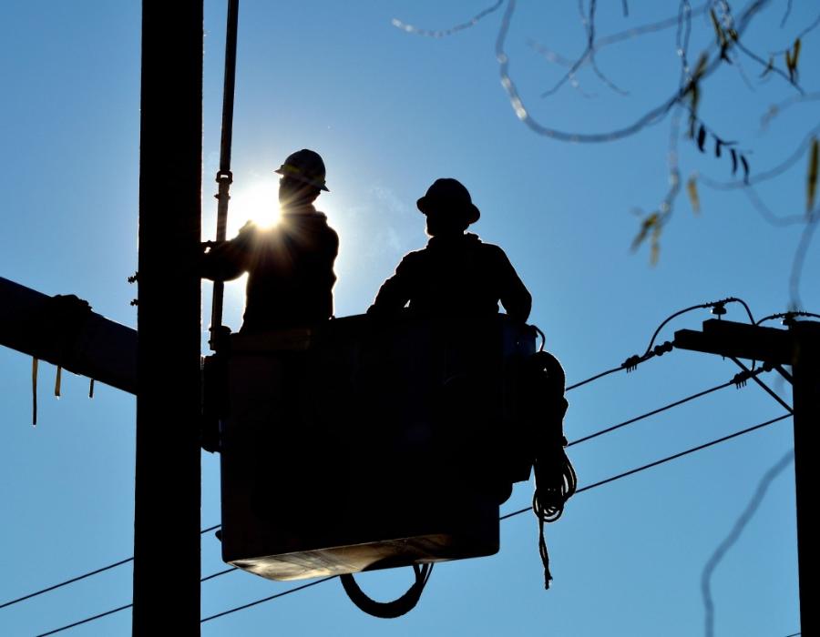 Silhouette of two lineman in a bucket doing repairs